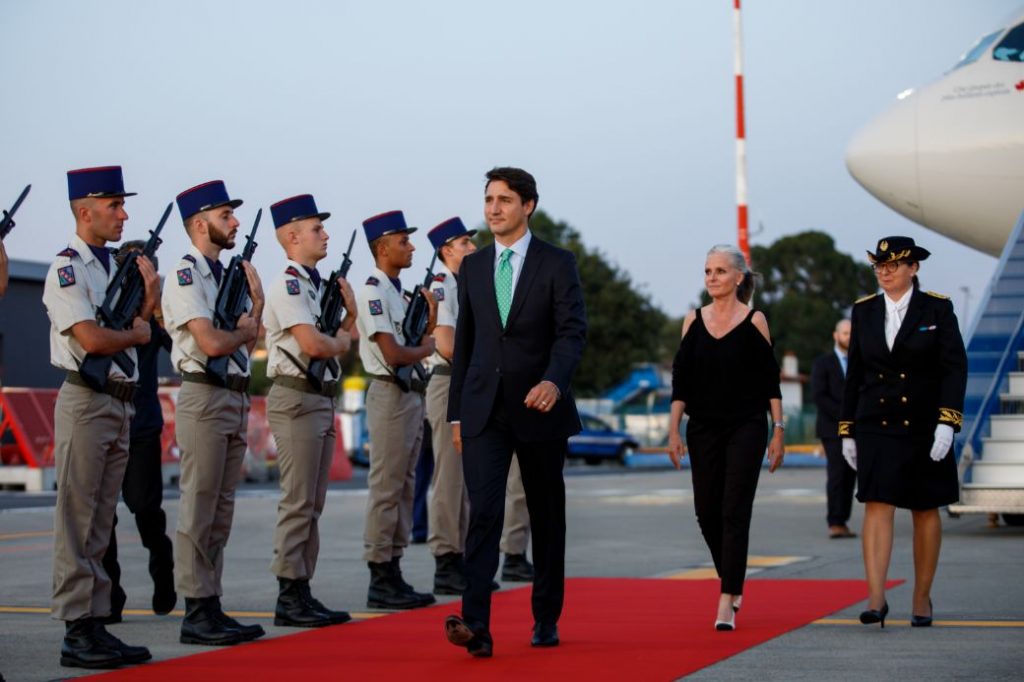 justin trudeau walks on a red carpet in front of a military guard